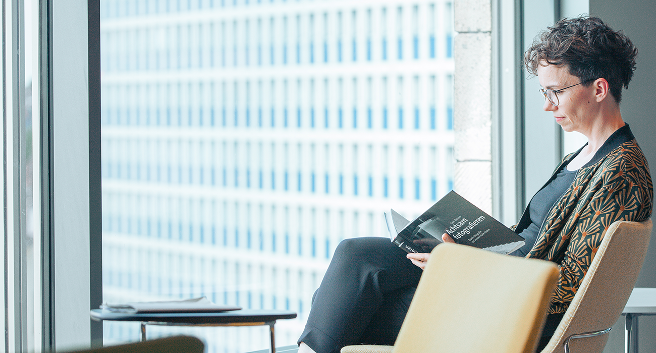 Verena Smit sitzt vor einem großen Fenster in einem Sessel und liest in einem Buch.