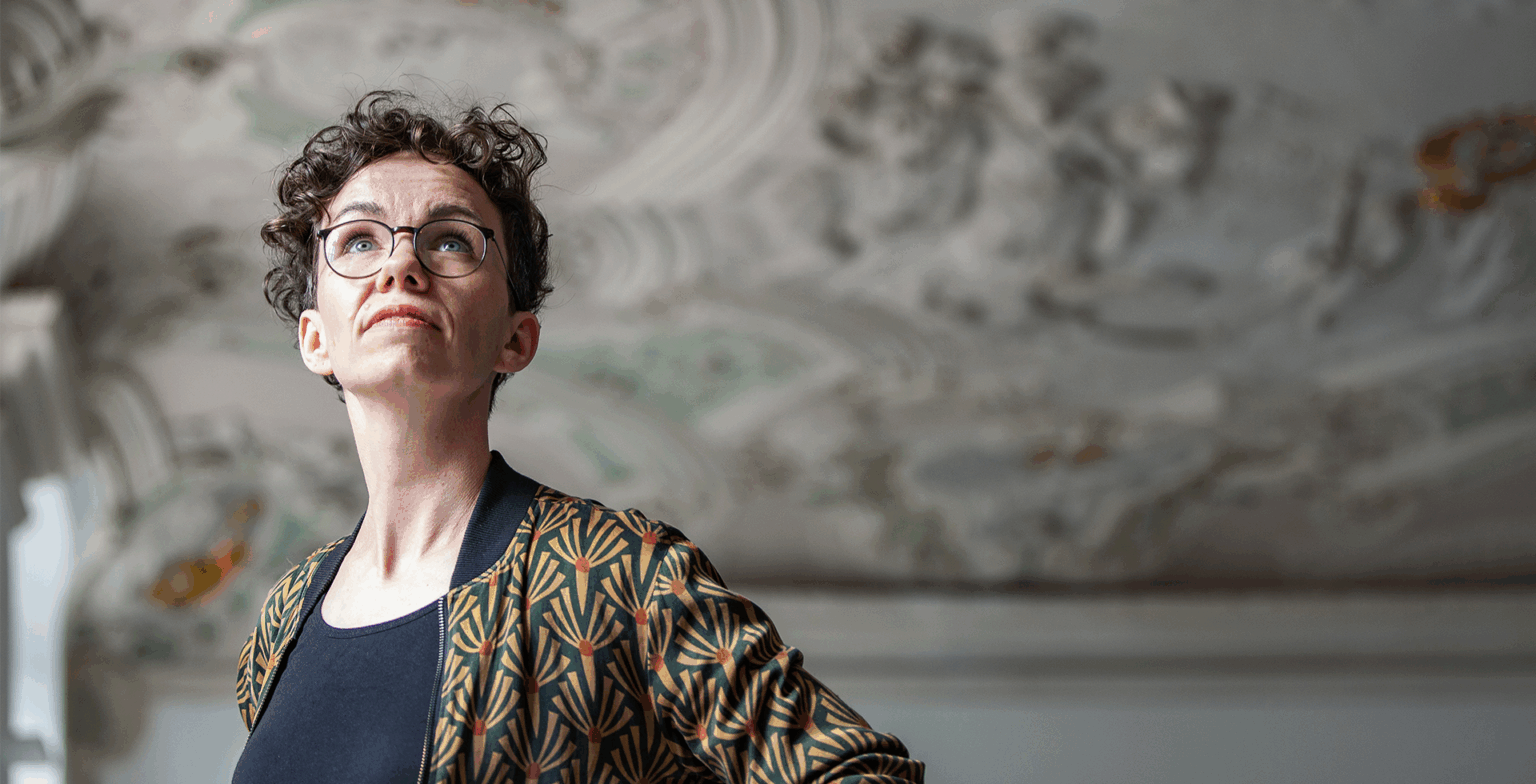 Verena Smit betrachtet die Stuckdecke eines historischen Gebäudes.